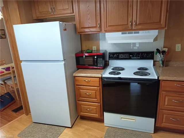 Kitchen with white appliances, light hardwood / wood-style flooring, and decorative backsplash