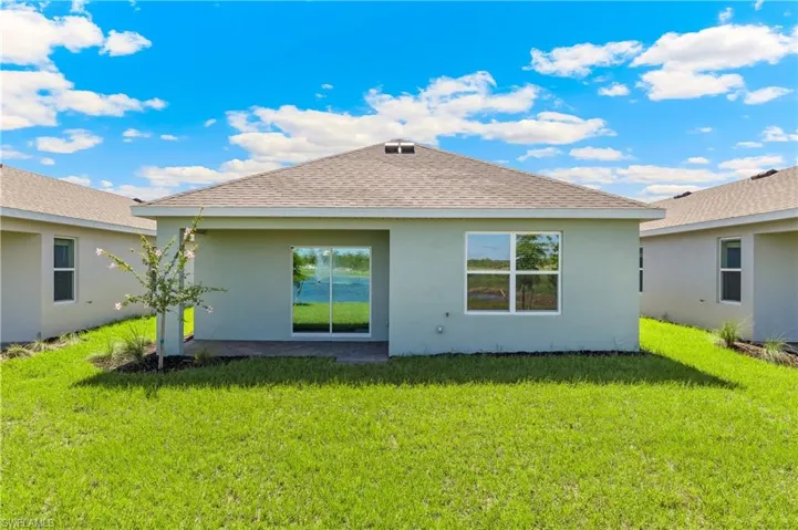 Back of property featuring roof with shingles, a lawn, and stucco siding