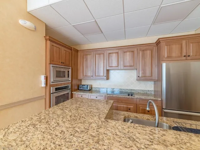 Kitchen featuring tasteful backsplash, a paneled ceiling, appliances with stainless steel finishes, and light stone counters