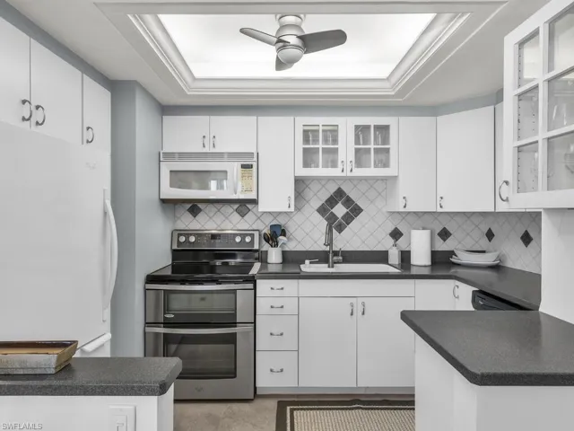 Kitchen featuring white cabinetry, a raised ceiling, and white appliances