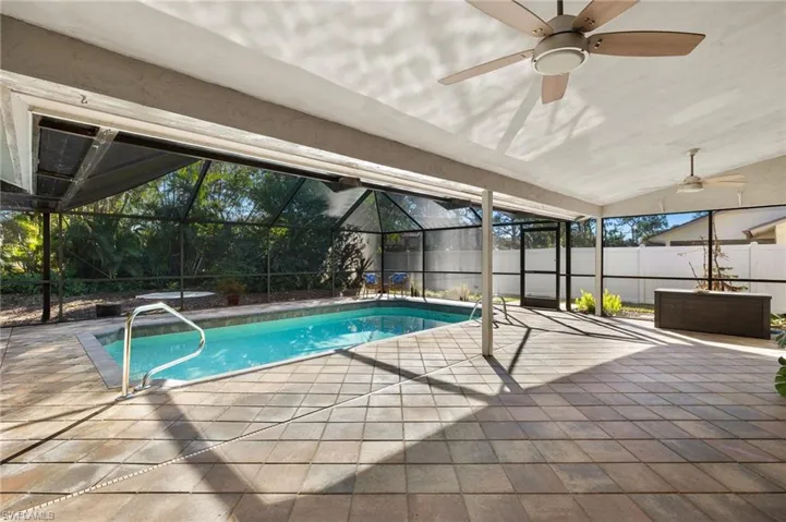 View of swimming pool featuring fence, a lanai, a patio area, and a ceiling fan