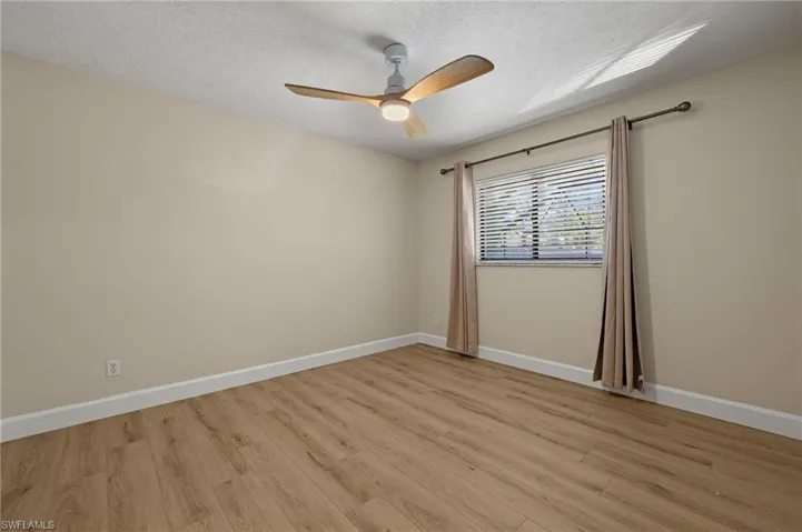 Empty room with baseboards, light wood-style floors, a textured ceiling, and ceiling fan