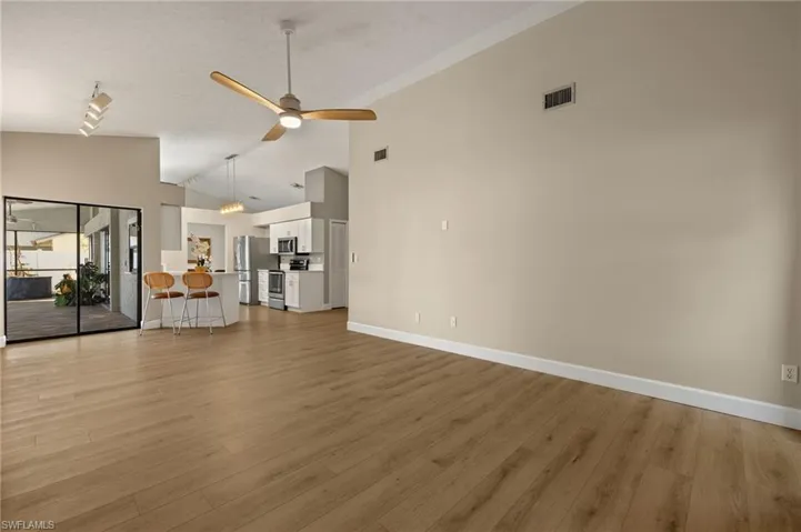 Unfurnished living room featuring high vaulted ceiling, baseboards, light wood finished floors, visible vents, and a ceiling fan