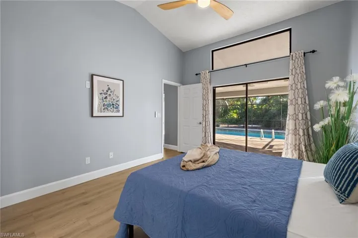Bedroom with high vaulted ceiling, baseboards, wood finished floors, a ceiling fan, and access to exterior