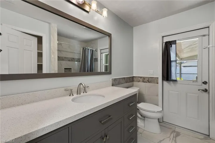 Full bathroom featuring tile walls, marble finish floor, toilet, vanity, and a shower with curtain