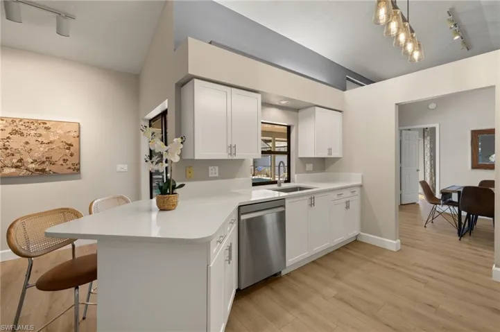 Kitchen with light countertops, a sink, light wood finished floors, a kitchen breakfast bar, and stainless steel dishwasher