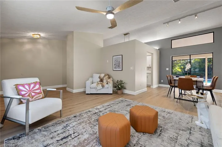 Living area featuring lofted ceiling, baseboards, a textured ceiling, a ceiling fan, and wood finished floors