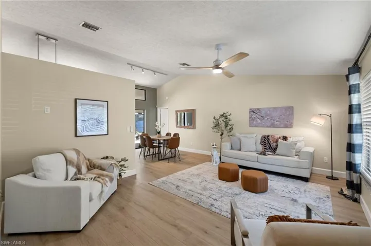 Living area with vaulted ceiling, a textured ceiling, visible vents, light wood-style floors, and ceiling fan