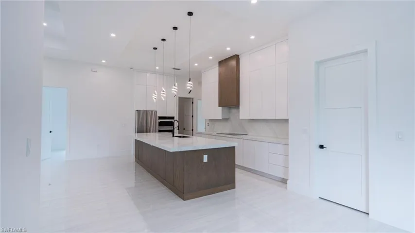 Modern kitchen featuring an expansive center island with a stone countertop, sleek white cabinetry, and a wood-finish range hood