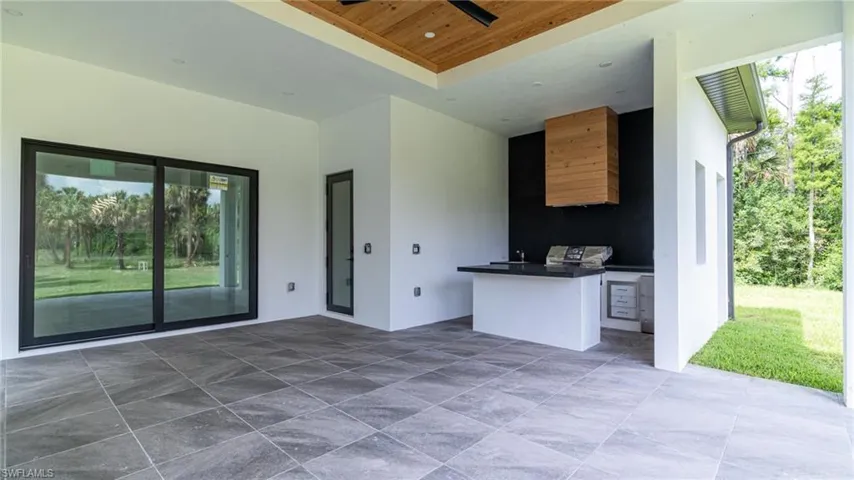Covered patio featuring an outdoor kitchen with integrated grill and beverage refrigerator, wood-finish ceiling, and dark gray porcelain tile flooring