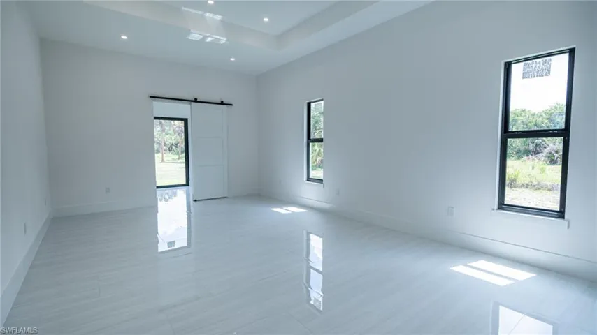 Spacious room featuring glossy tile flooring, recessed ceiling lighting, a tray ceiling, and a modern barn door
