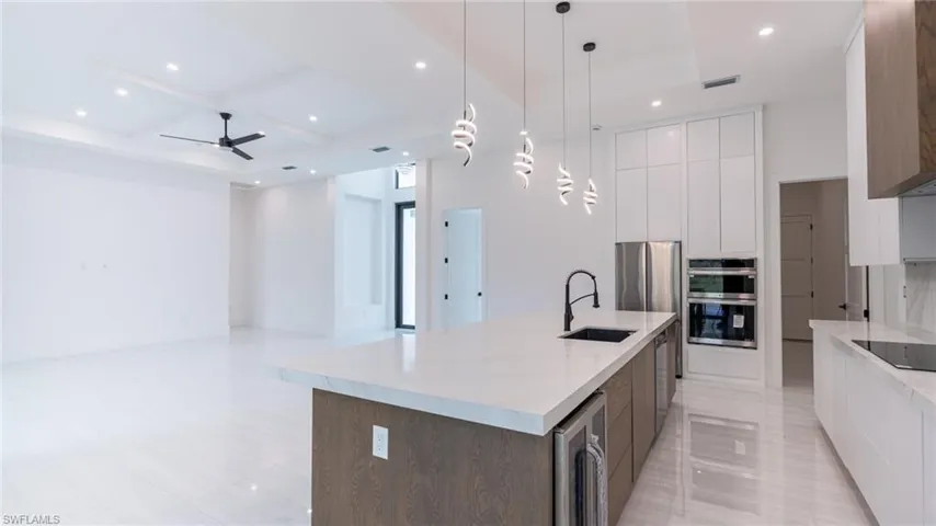 Open-concept kitchen and living area featuring a large center island with integrated sink and beverage cooler, stainless steel appliances, white flat-panel cabinetry, and recessed lighting