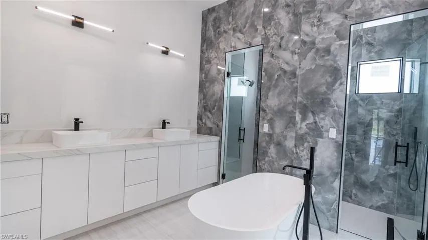 Spacious bathroom featuring a white freestanding soaking tub, dual glass-enclosed showers, and a double vanity with white cabinetry and rectangular vessel sinks