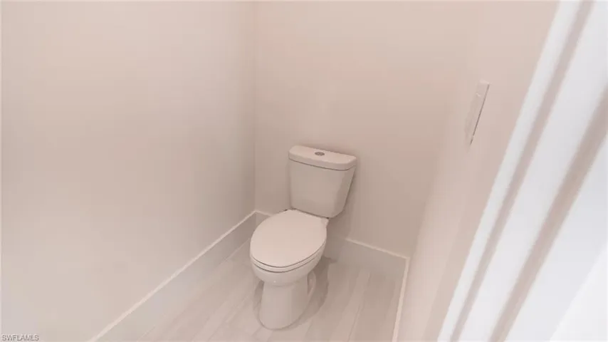 Powder room featuring a white toilet, light-toned walls, and wood-finish flooring with white baseboards