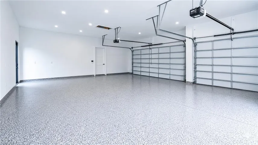 Spacious garage featuring a durable epoxy floor finish, recessed ceiling lighting, two automatic garage doors, and a pedestrian door