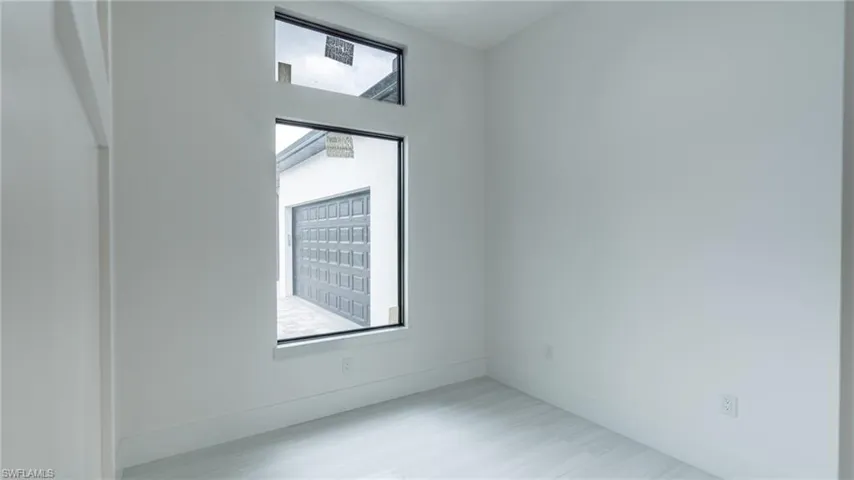 Bright interior room featuring a large rectangular window with transom, light wood-finish flooring, and crisp white walls