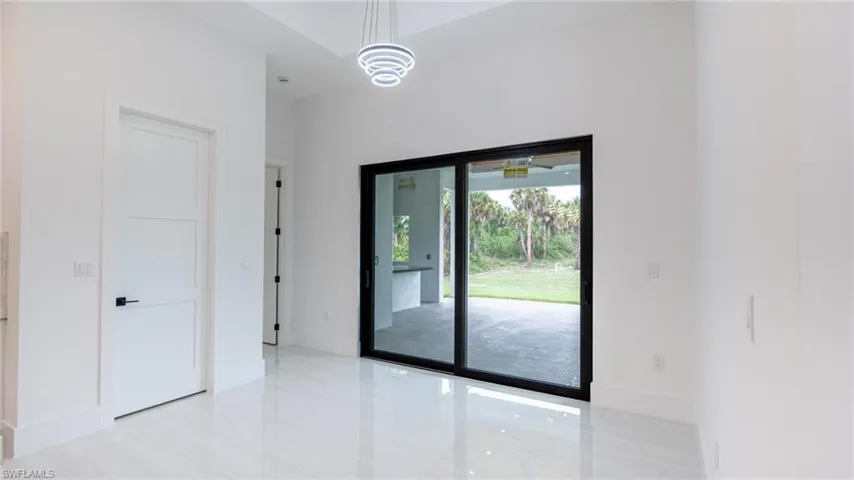 Spacious interior featuring a large sliding glass door, high ceilings, bright white walls, polished tile flooring, and a contemporary chandelier