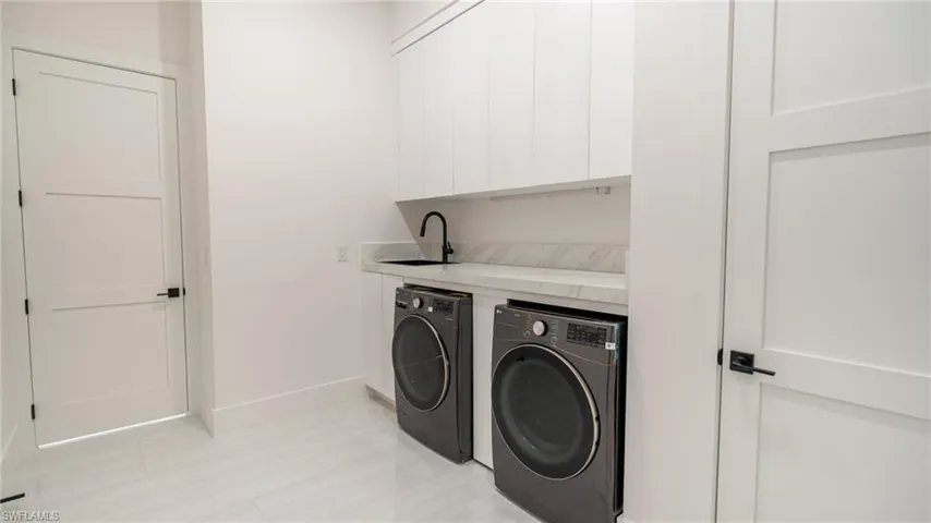 Contemporary laundry room featuring white cabinetry, light-toned countertop, and a matte black faucet over a black sink