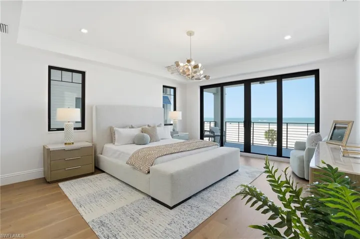 Bedroom with a water view, a tray ceiling, access to exterior, light wood-style floors, and suspended lighting