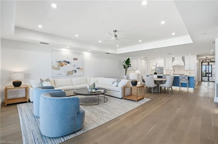Living room featuring a tray ceiling, light wood-style flooring, a ceiling fan, and recessed lighting