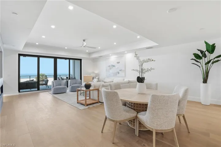 Dining area with a tray ceiling, a ceiling fan, light wood-type flooring, recessed lighting, and a water view