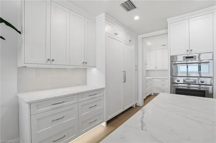 Kitchen with light stone countertops, white cabinets, stainless steel double oven, dark wood finished floors, and recessed lighting