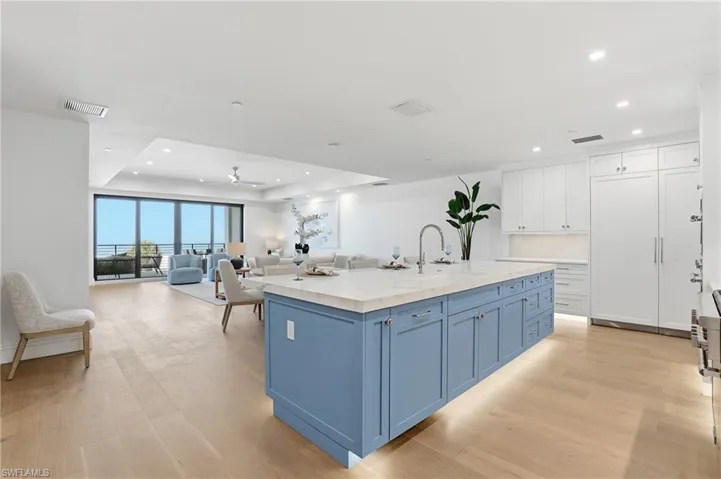 Kitchen featuring an island with sink, two tone cabinetry, open floor plan, a ceiling fan, and a tray ceiling
