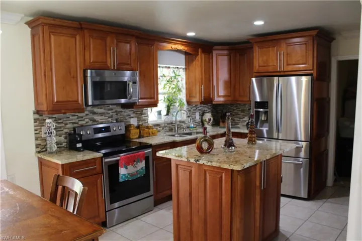 Kitchen featuring brown cabinetry, appliances with stainless steel finishes, light stone counters, light tile patterned floors, and a center island
