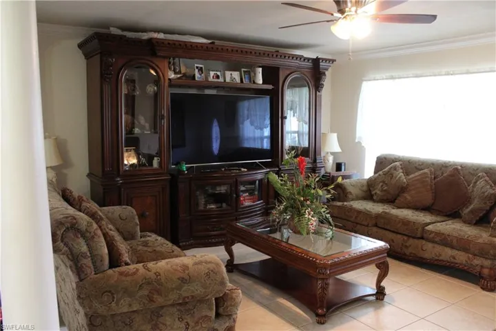 Living area with crown molding, tile patterned flooring, and a ceiling fan