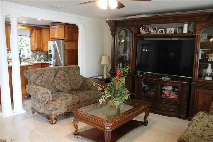 Living area featuring a ceiling fan, light tile patterned floors, ornamental molding, and ornate columns
