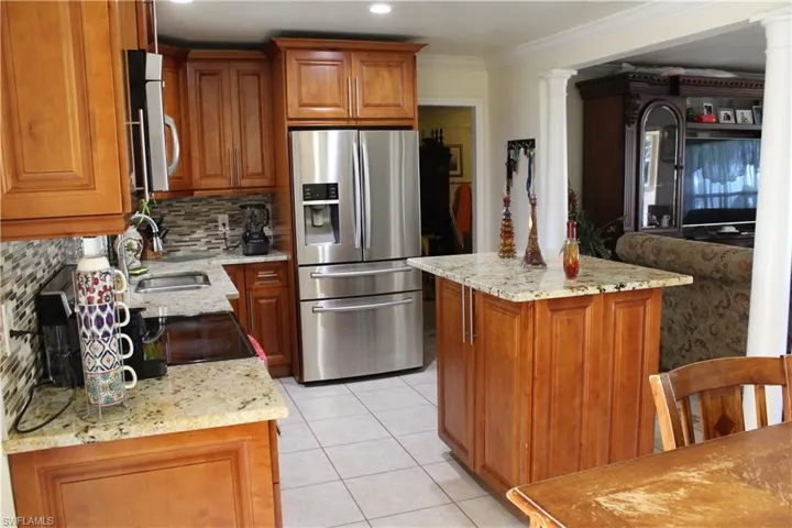 Kitchen with brown cabinetry, stainless steel appliances, light stone counters, decorative backsplash, and crown molding