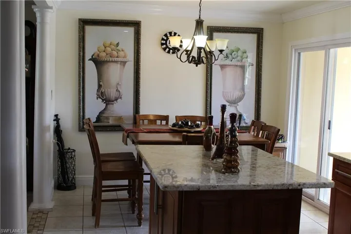 Kitchen with dark brown cabinetry, decorative columns, hanging light fixtures, light stone countertops, and a kitchen island