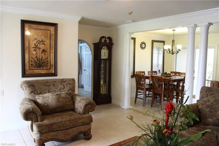 Living room with ornate columns, light tile patterned floors, crown molding, and a chandelier