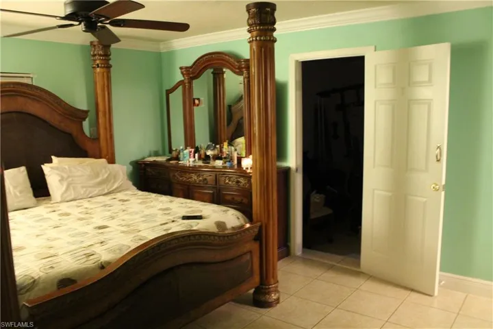 Bedroom featuring light tile patterned floors, a ceiling fan, ornamental molding, and a spacious closet