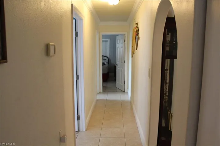 Hallway featuring light tile patterned floors, ornamental molding, and arched walkways