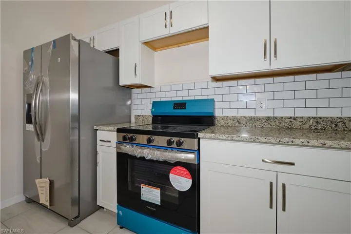 Kitchen with light stone counters, white cabinets, light tile patterned floors, backsplash, and appliances with stainless steel finishes