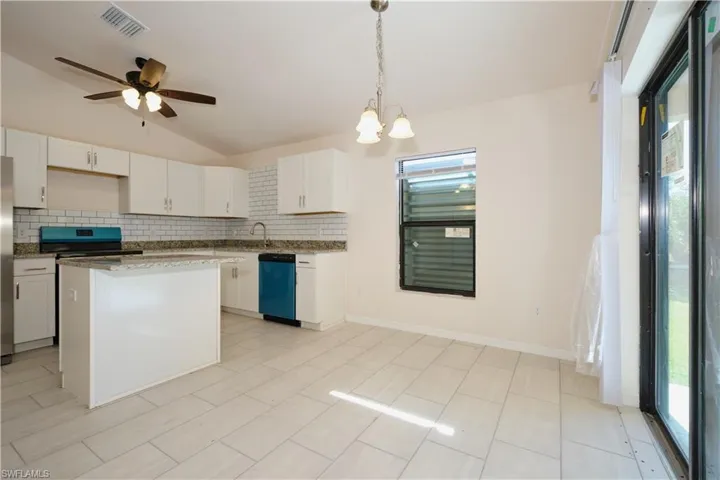 Kitchen featuring white cabinetry, appliances with stainless steel finishes, vaulted ceiling, and a center island