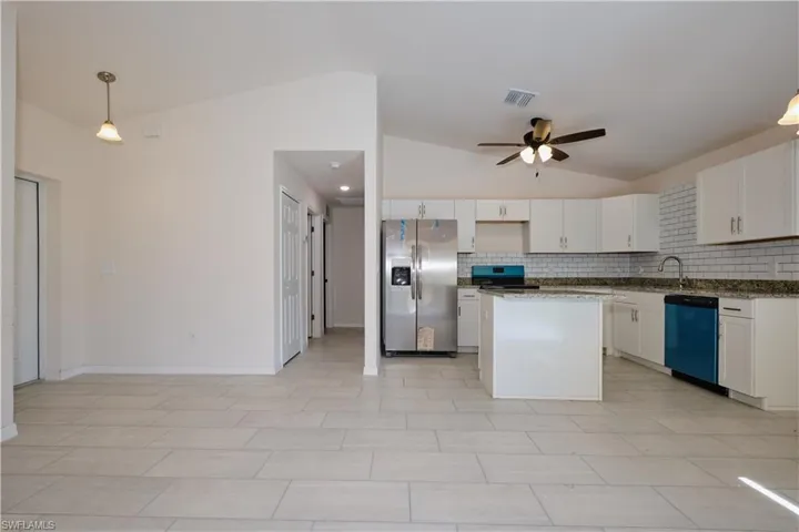 Kitchen featuring stainless steel appliances, a center island, vaulted ceiling, white cabinets, and decorative light fixtures