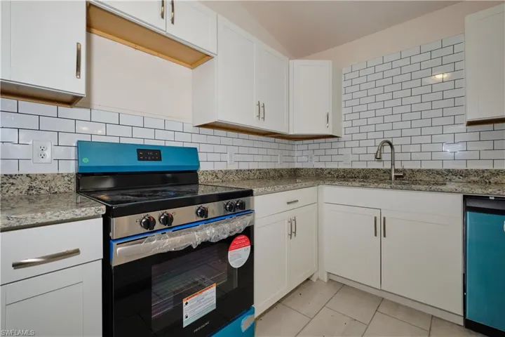 Kitchen with tasteful backsplash, white cabinetry, appliances with stainless steel finishes, and light stone counters