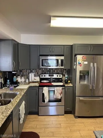 Kitchen with refrigerator, light stone countertops, backsplash, and range