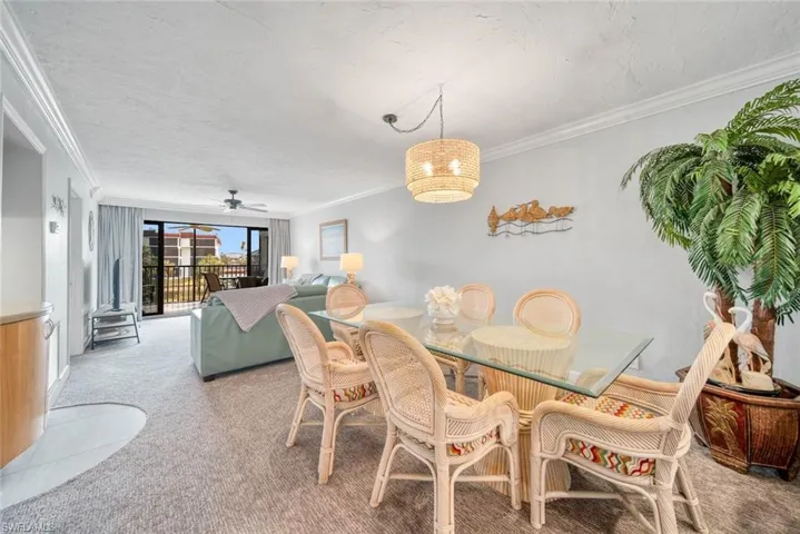 Carpeted dining room featuring ceiling fan, ornamental molding, and a textured ceiling
