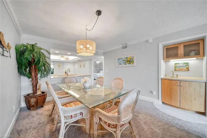 Carpeted dining space featuring ornamental molding, sink, and ceiling fan with notable chandelier
