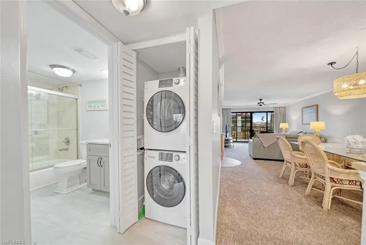 Clothes washing area with stacked washing maching and dryer, crown molding, light carpet, and ceiling fan