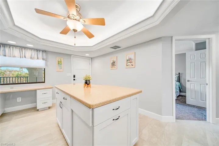 Kitchen featuring ornamental molding, white cabinets, built in desk, and a raised ceiling