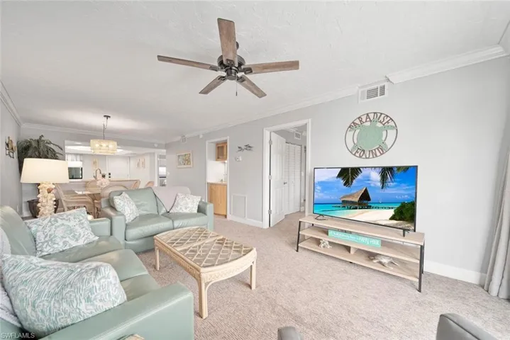 Carpeted living room with crown molding, a textured ceiling, and ceiling fan with notable chandelier