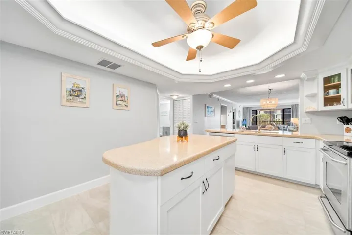 Kitchen with white cabinets, kitchen peninsula, a tray ceiling, and electric stove