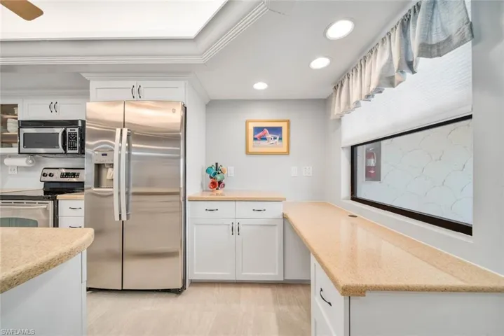 Kitchen with ornamental molding, appliances with stainless steel finishes, light wood-type flooring, and white cabinets