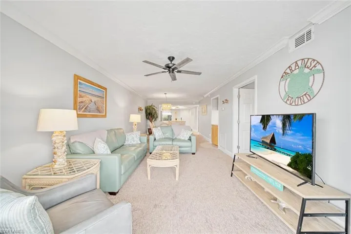 Carpeted living room featuring ornamental molding and ceiling fan