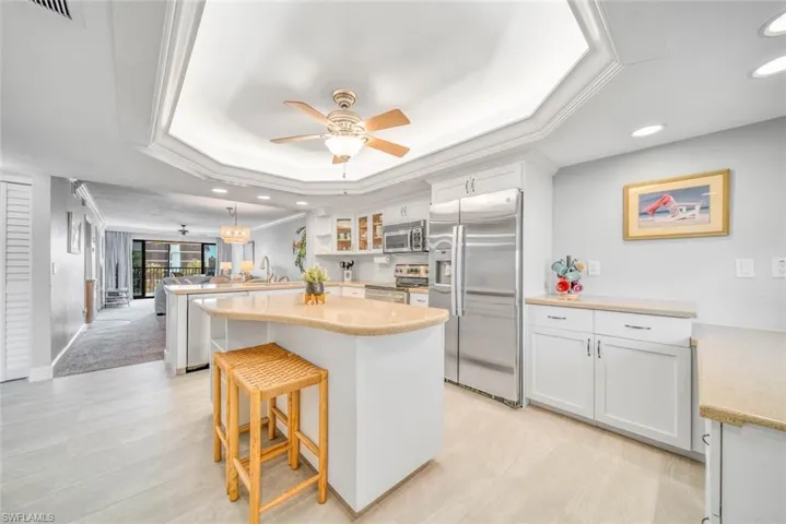 Kitchen featuring kitchen peninsula, a tray ceiling, a center island, white cabinetry, and appliances with stainless steel finishes