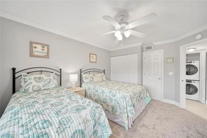 Bedroom with stacked washer and dryer, a closet, ornamental molding, light colored carpet, and ceiling fan